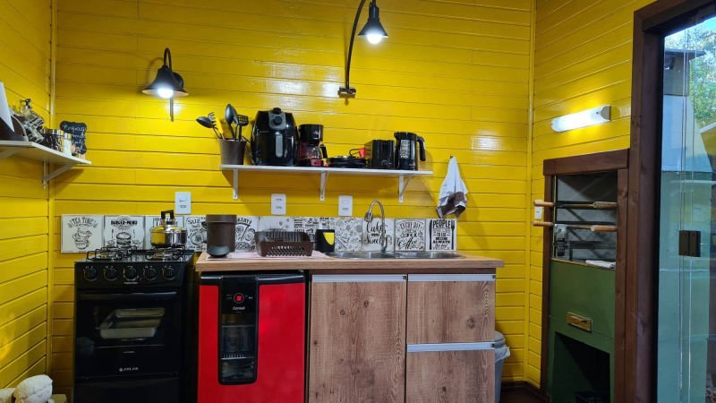 Cozinha do espaço gourmet com paredes amarelas, fogão, frigobar e pia