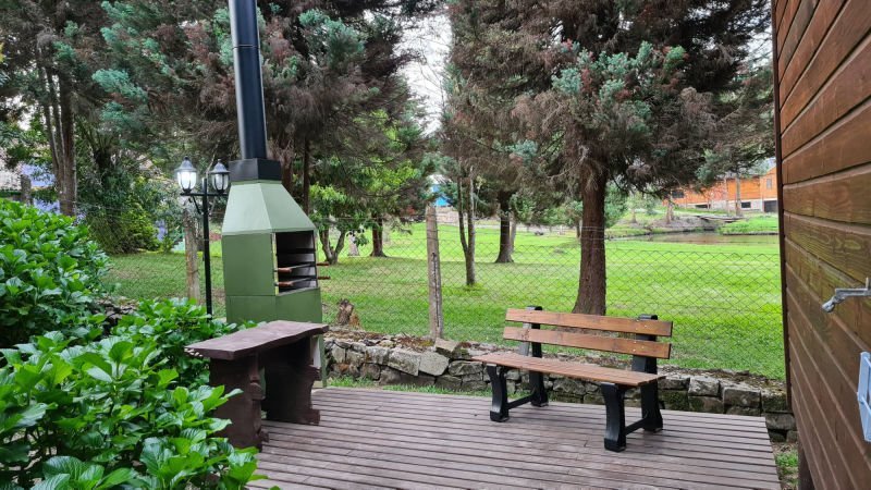 Churrasqueira e banco de madeira em deck coberto, de frente para o gramado