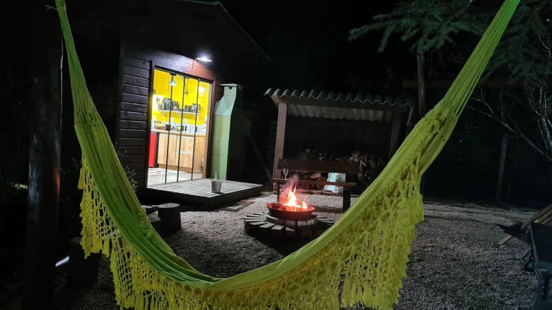 Rede amarela e fogueira acesa em frente ao espaço gourmet iluminado à noite